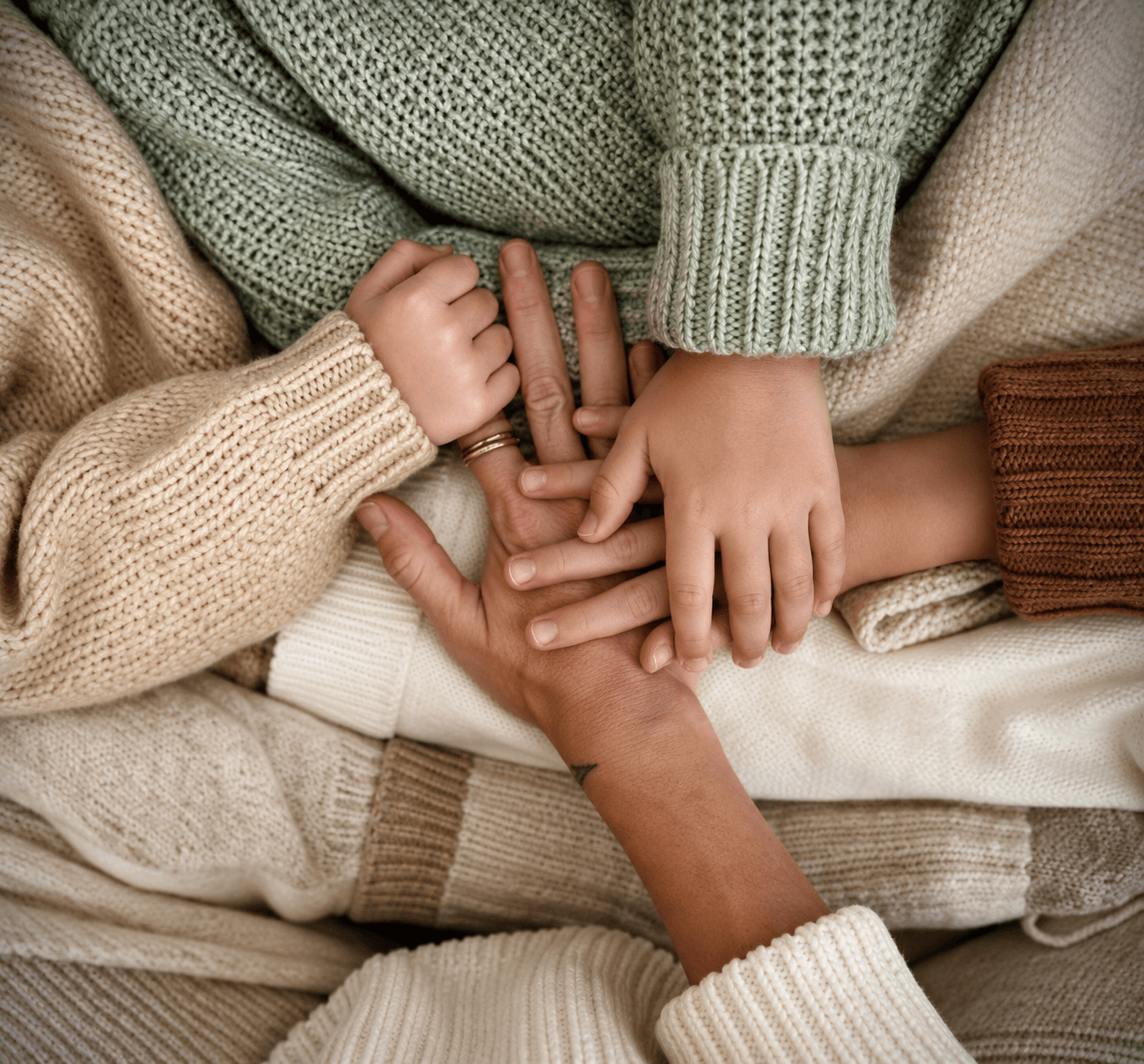 Manos de dos adultos y una criatura entrelazadas sobre una manta