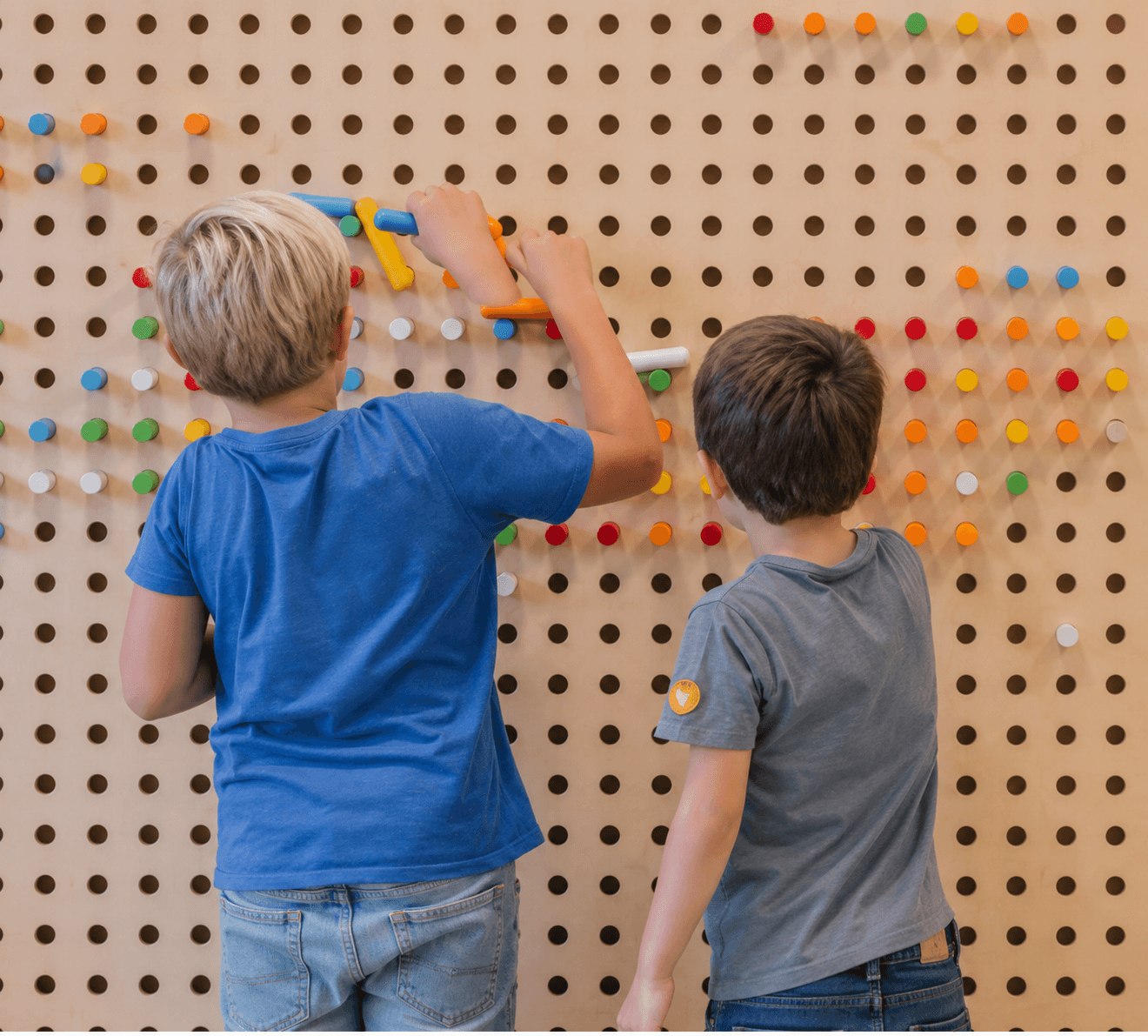 Dos niños encajando piezas de colores en un panel perforado