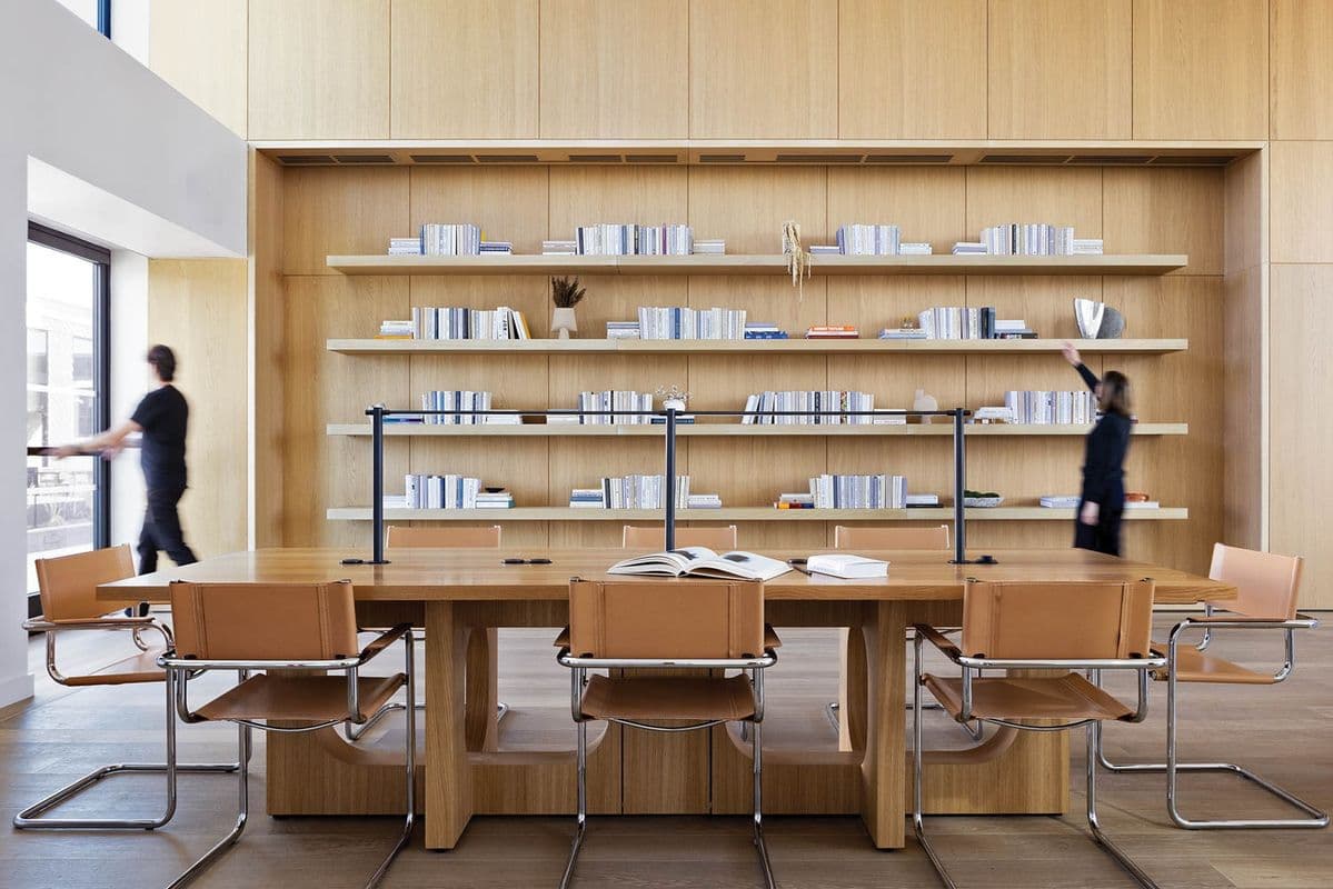 Sala de reuniones con una mesa larga de madera clara, sillas de cuero y una pared de estanterías con libros